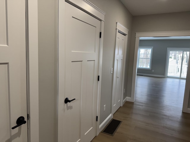 hallway with baseboards, visible vents, and wood finished floors