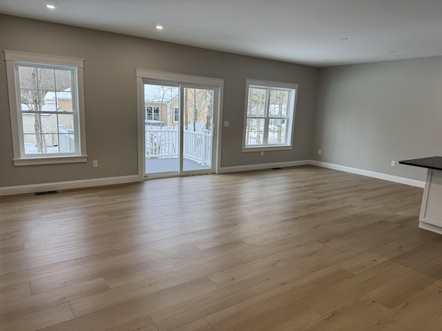 unfurnished living room featuring a wealth of natural light, baseboards, and light wood finished floors