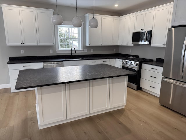 kitchen featuring dark countertops, a kitchen island, appliances with stainless steel finishes, and a sink