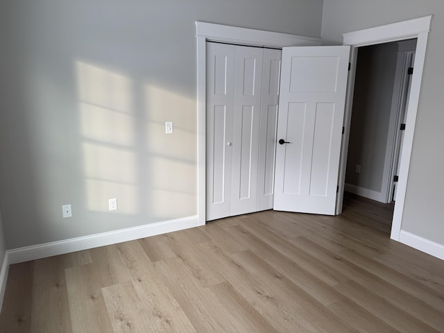 unfurnished bedroom featuring a closet, light wood-style flooring, and baseboards