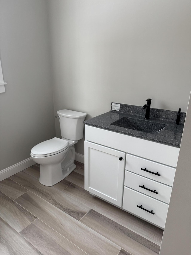 bathroom featuring baseboards, vanity, toilet, and wood finished floors