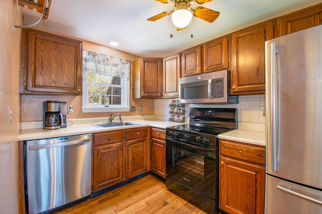 kitchen featuring appliances with stainless steel finishes, brown cabinetry, a sink, light countertops, and light wood-type flooring