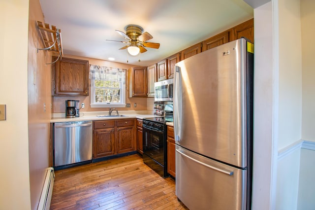 kitchen with a sink, brown cabinetry, stainless steel appliances, a ceiling fan, and baseboard heating