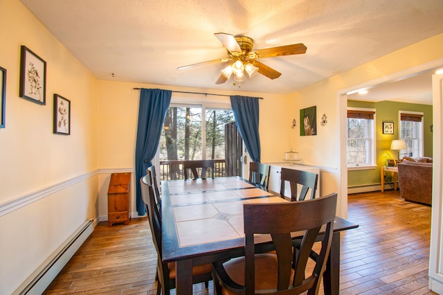 dining room with a ceiling fan, a baseboard heating unit, and hardwood / wood-style flooring