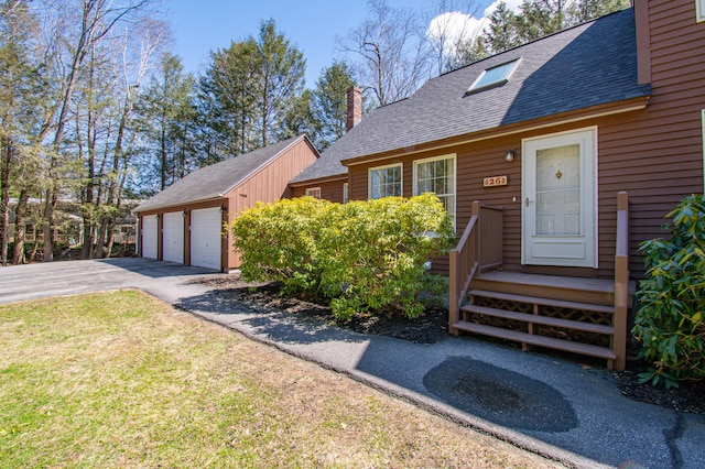 view of front of home featuring roof with shingles, a detached garage, an outbuilding, a front lawn, and a chimney