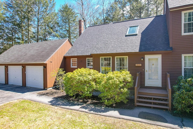 new england style home with an outbuilding, roof with shingles, and a chimney