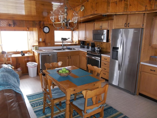 kitchen with appliances with stainless steel finishes, light tile floors, sink, a chandelier, and wooden walls