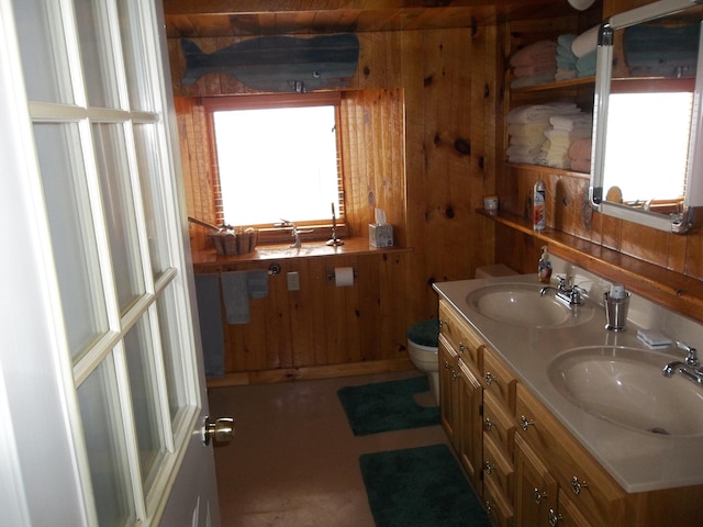 bathroom featuring a healthy amount of sunlight, wooden walls, toilet, and vanity with extensive cabinet space