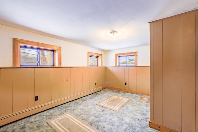 empty room featuring wainscoting, wood walls, and a baseboard radiator