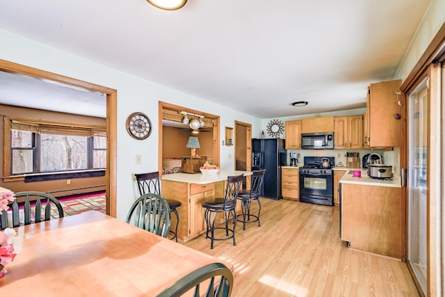 kitchen with light wood-style floors, a breakfast bar area, light countertops, and black appliances