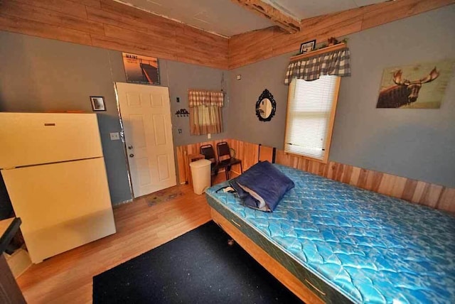 bedroom featuring white fridge, beam ceiling, and light hardwood / wood-style flooring