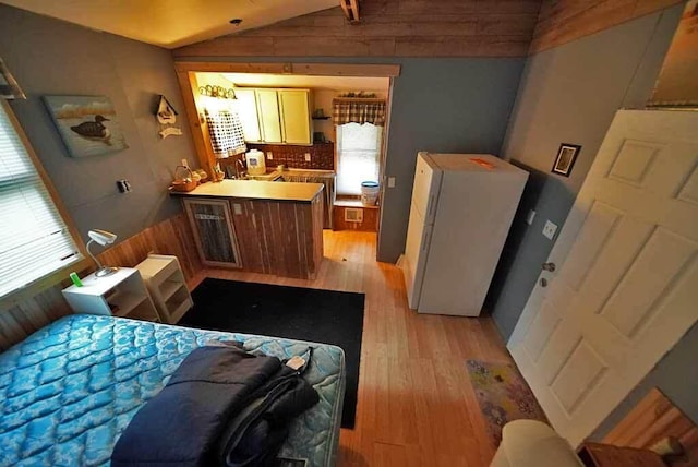 bedroom featuring lofted ceiling, light hardwood / wood-style flooring, and white refrigerator