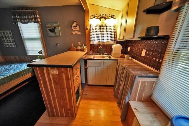 kitchen with backsplash, light hardwood / wood-style flooring, sink, and kitchen peninsula