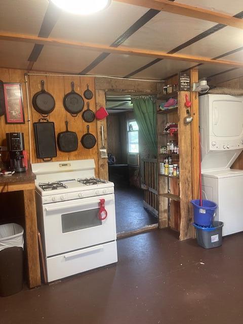 kitchen featuring wood walls, stacked washer and clothes dryer, white gas range, and concrete flooring