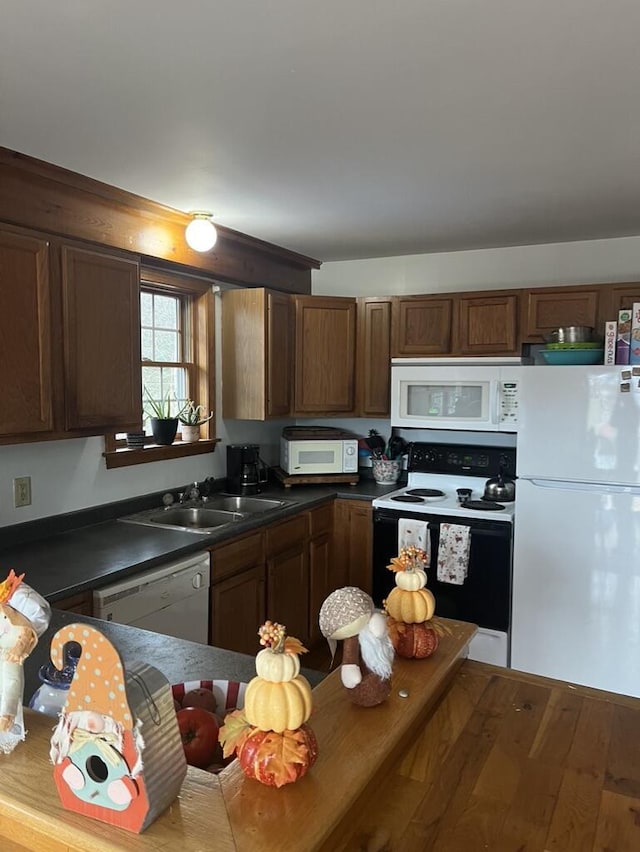 kitchen featuring white appliances, hardwood / wood-style floors, a sink, dark countertops, and brown cabinetry