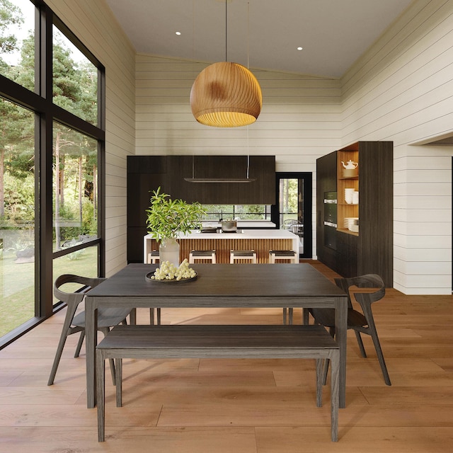 dining room with a towering ceiling, wooden walls, and light wood finished floors