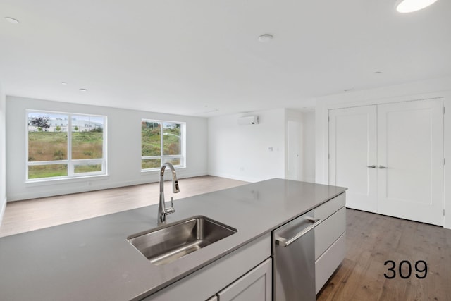 kitchen with a wall unit AC, white cabinetry, wood-type flooring, dishwasher, and sink