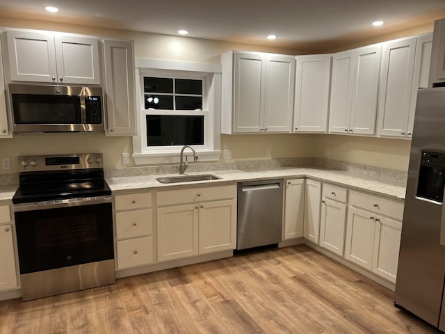 kitchen with sink, white cabinets, stainless steel appliances, and light hardwood / wood-style flooring