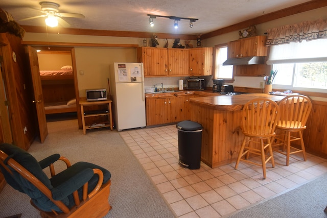 kitchen featuring light tile floors, white fridge, ceiling fan, and a breakfast bar area