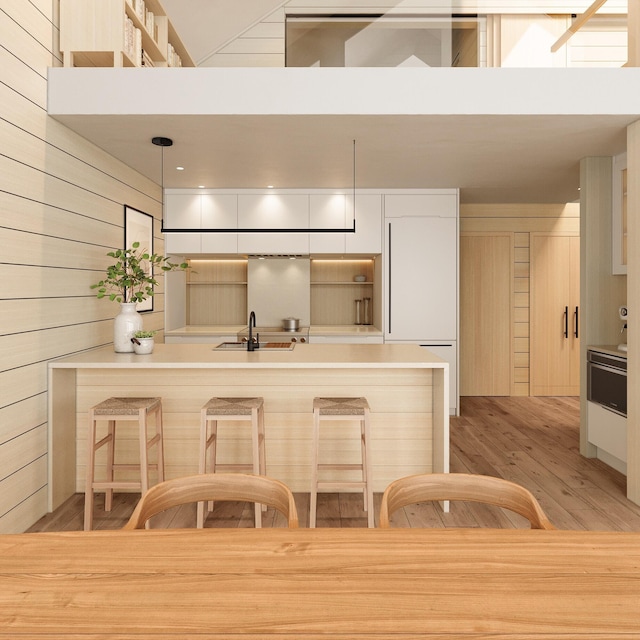 kitchen featuring sink, wooden walls, a towering ceiling, light hardwood / wood-style flooring, and pendant lighting