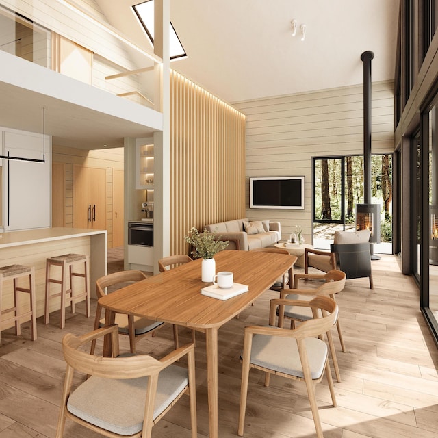 dining space featuring high vaulted ceiling, light wood-type flooring, a wood stove, and wooden walls