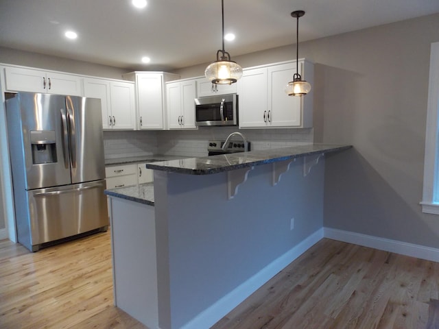 kitchen with appliances with stainless steel finishes, tasteful backsplash, kitchen peninsula, light hardwood / wood-style flooring, and hanging light fixtures