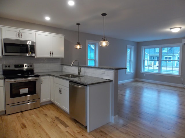 kitchen with pendant lighting, sink, white cabinets, light hardwood / wood-style flooring, and stainless steel appliances