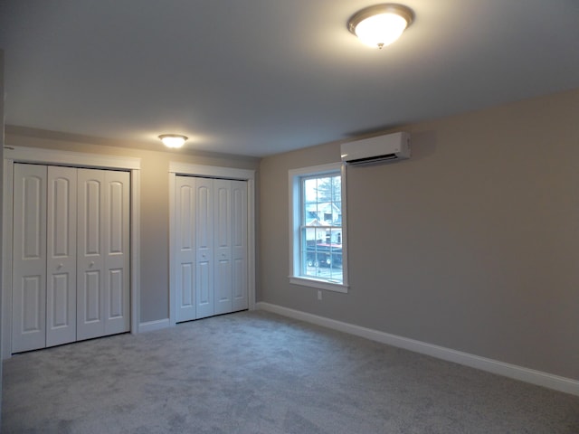 unfurnished bedroom featuring light carpet, two closets, and a wall unit AC