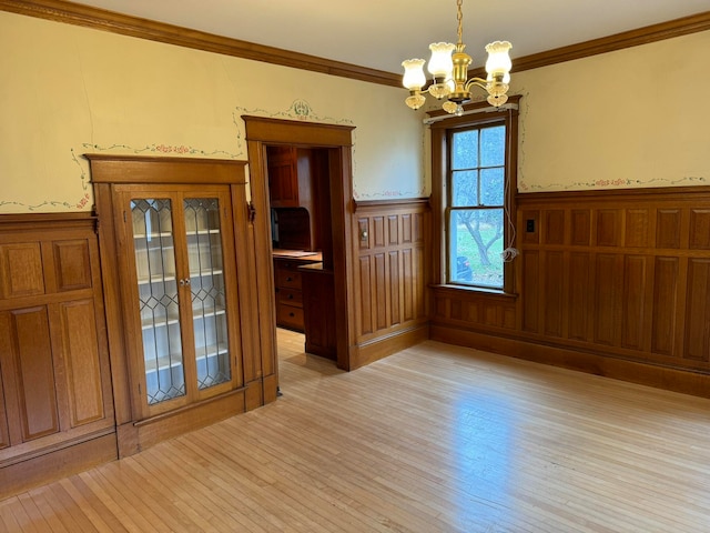 empty room with crown molding, light hardwood / wood-style floors, and an inviting chandelier