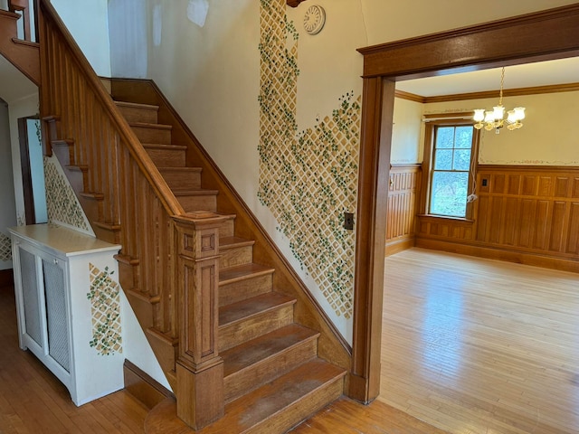 stairway with a chandelier, wooden walls, ornamental molding, and light wood-type flooring