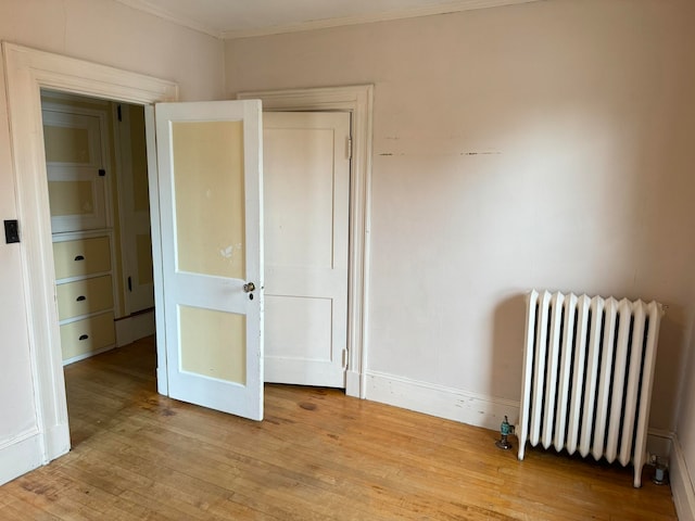 unfurnished bedroom with crown molding, light hardwood / wood-style floors, and radiator