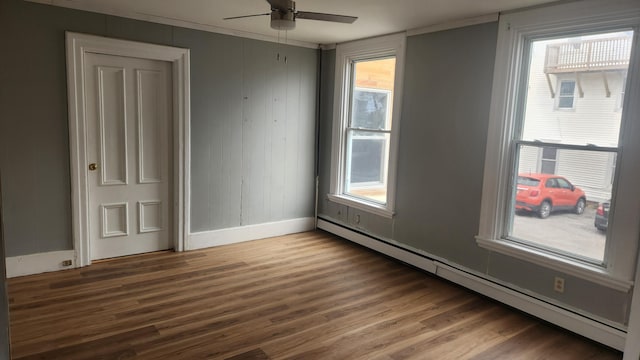 spare room featuring a healthy amount of sunlight, ceiling fan, wood-type flooring, and a baseboard heating unit