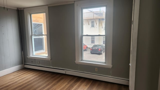 spare room with a wealth of natural light, wood-type flooring, and a baseboard heating unit