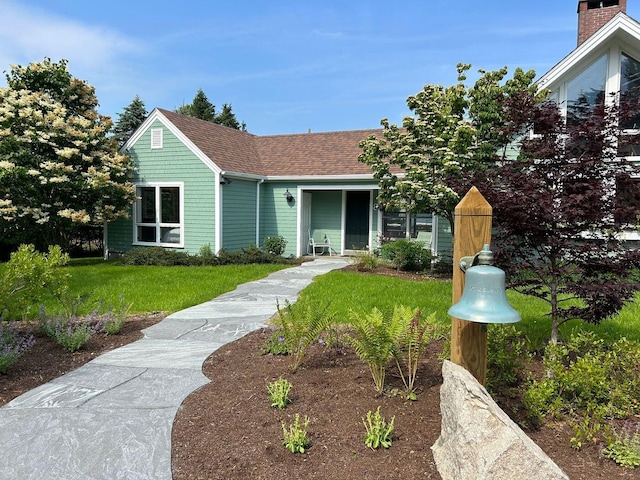 view of front facade with a shingled roof and a front yard