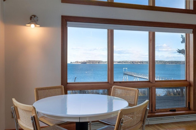 dining space featuring a water view, hardwood / wood-style flooring, a baseboard radiator, and a wealth of natural light