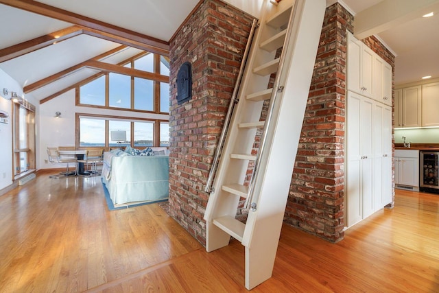 interior space featuring light hardwood / wood-style flooring, lofted ceiling with beams, beverage cooler, and brick wall