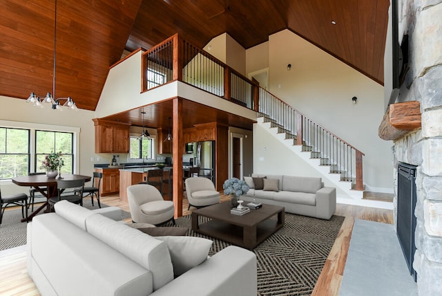 living room featuring an inviting chandelier, high vaulted ceiling, wooden ceiling, a fireplace, and light hardwood / wood-style floors