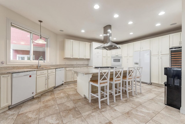 kitchen with white appliances, light stone counters, island range hood, a center island, and decorative light fixtures