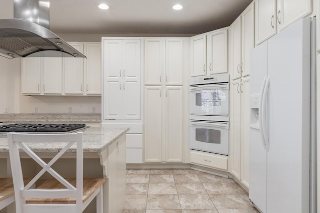 kitchen with white appliances, light stone countertops, island exhaust hood, and white cabinetry