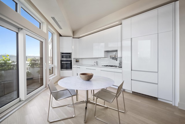 dining space with light wood-type flooring, vaulted ceiling, and sink