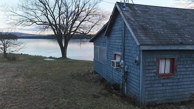 view of property exterior with an outbuilding, a yard, roof with shingles, and a water view