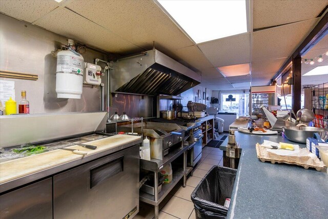 kitchen featuring washer / dryer, light tile patterned floors, exhaust hood, and a drop ceiling