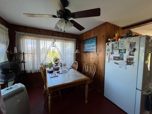 dining room featuring ceiling fan and wooden walls