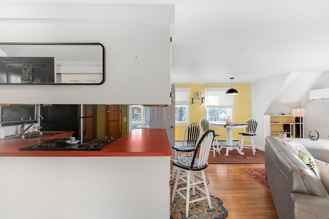 kitchen featuring pendant lighting, sink, hardwood / wood-style floors, a wall mounted AC, and black electric cooktop