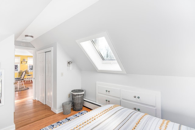 bedroom with a baseboard heating unit, vaulted ceiling with skylight, light wood-type flooring, and a closet