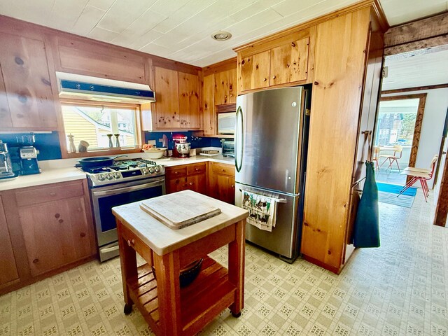 kitchen with appliances with stainless steel finishes, light countertops, extractor fan, light floors, and brown cabinetry