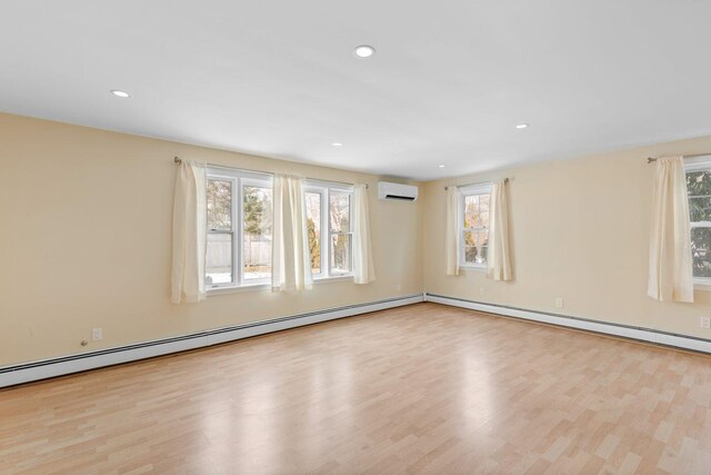 spare room with a wall mounted AC, light hardwood / wood-style floors, and a wealth of natural light