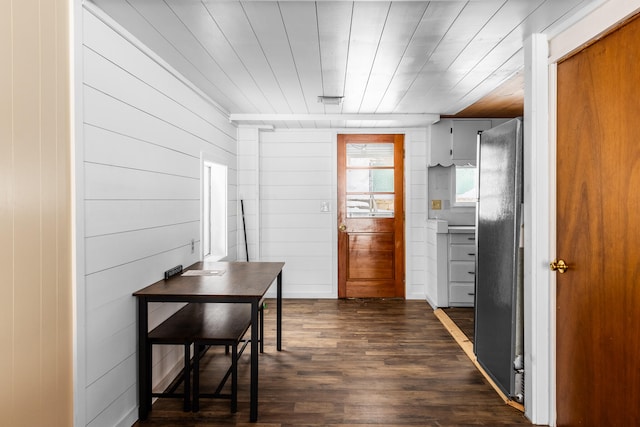 kitchen featuring black fridge, dark wood-type flooring, wooden walls, and wood ceiling