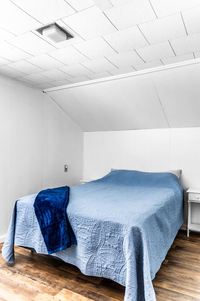 bedroom with wooden walls, vaulted ceiling, and dark hardwood / wood-style floors