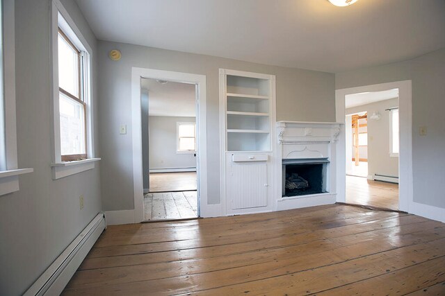 unfurnished living room featuring built in shelves, light wood-type flooring, and baseboard heating